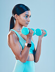 Fitness, workout and woman with weights in a studio for a arm or strength training with motivation. Sports, health and Indian female athlete or model doing exercise while isolated by blue background.