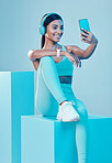 Woman, fitness and selfie in studio with headphones, wellness and training clothes by background. Gen z model, training and fashion with streaming music, body goals or exercise for health by backdrop