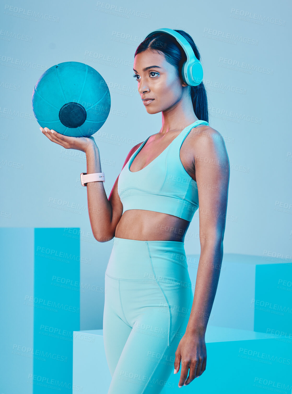 Buy stock photo Fitness, ball and woman in studio with music for training, exercise and sports routine on blue background. Headphones, radio and Indian female athlete with weight and podcast, mindset and focus 