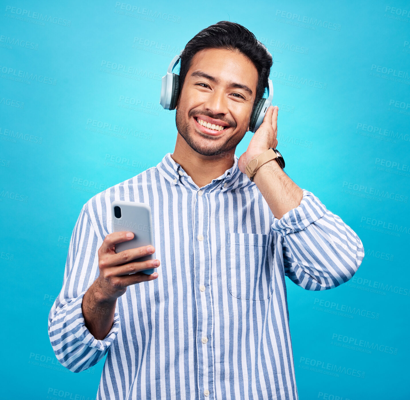 Buy stock photo Happy man in portrait, smartphone and headphones, listen to music with entertainment on blue background. Male person with smile, wireless technology and online audio streaming with radio or podcast