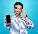 Asian man, phone and mockup screen with earphones for music listening, call or audio against a blue studio background. Portrait of happy male showing smartphone display for sound app or communication