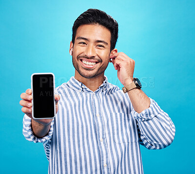 Buy stock photo Asian man, phone and mockup screen with earphones for music listening, call or audio against a blue studio background. Portrait of happy male showing smartphone display for sound app or communication