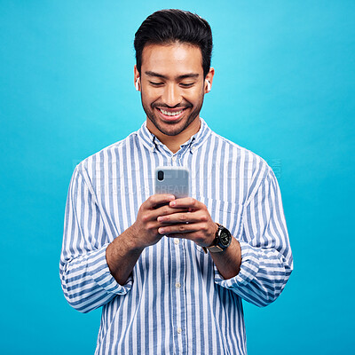 Buy stock photo Happy man, smartphone and earphones, music and social media with entertainment and chat on blue background. Male person with smile, wireless technology and online audio streaming with texting on app