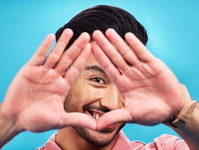 Buy stock photo Frame, hands and portrait of Asian man on blue background with smile, confidence and happiness. Perspective, framing and face of happy male in studio for photography, profile picture and vision sign