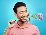 Teeth, flower and wink with portrait of man in studio for celebration, gift and romance. Funny, goofy and present with male isolated on blue background for happiness, smile and valentines day mockup