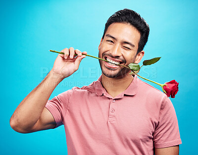 Buy stock photo Teeth, rose and wink with portrait of man in studio for celebration, gift and romance. Funny, goofy and present with male and flower on blue background for happiness, smile and valentines day mockup