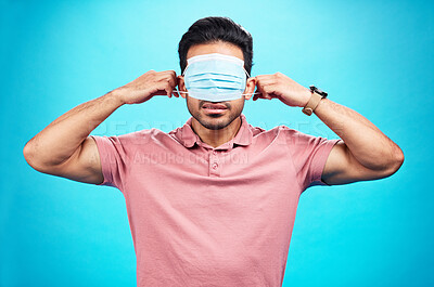 Buy stock photo Face mask, cover eyes and a man with blindfold isolated on a blue background in a studio. Struggling, virus and a person with covid wearing a tool to protect from sickness, hiding facial sight