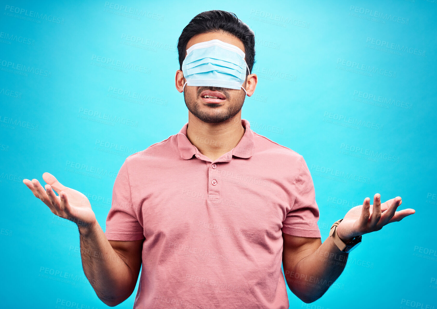 Buy stock photo Face mask, covid and man in blindfold shrugging in studio for doubt, medical misinformation or conspiracy theory. Confusion, virus or person with ppe isolated on blue background for pandemic question