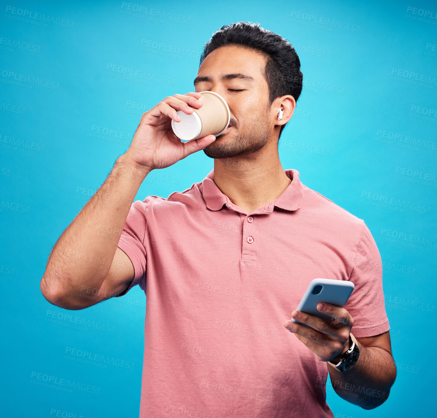 Buy stock photo Earphones, drinking coffee and man with phone in studio isolated on a blue background. Tea, cellphone and Asian person drink, caffeine or espresso with mobile for social media, radio music or podcast