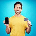 Portrait, phone and credit card for ecommerce with a man customer on a blue background in studio. Happy, smile and online shopping with a young shopper using fintech to make a payment or transaction