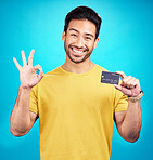 Ok, credit card and man in portrait isolated on blue background for shopping, e commerce and payment loan. Happy asian person, excited for banking solution, financial savings and okay emoji in studio