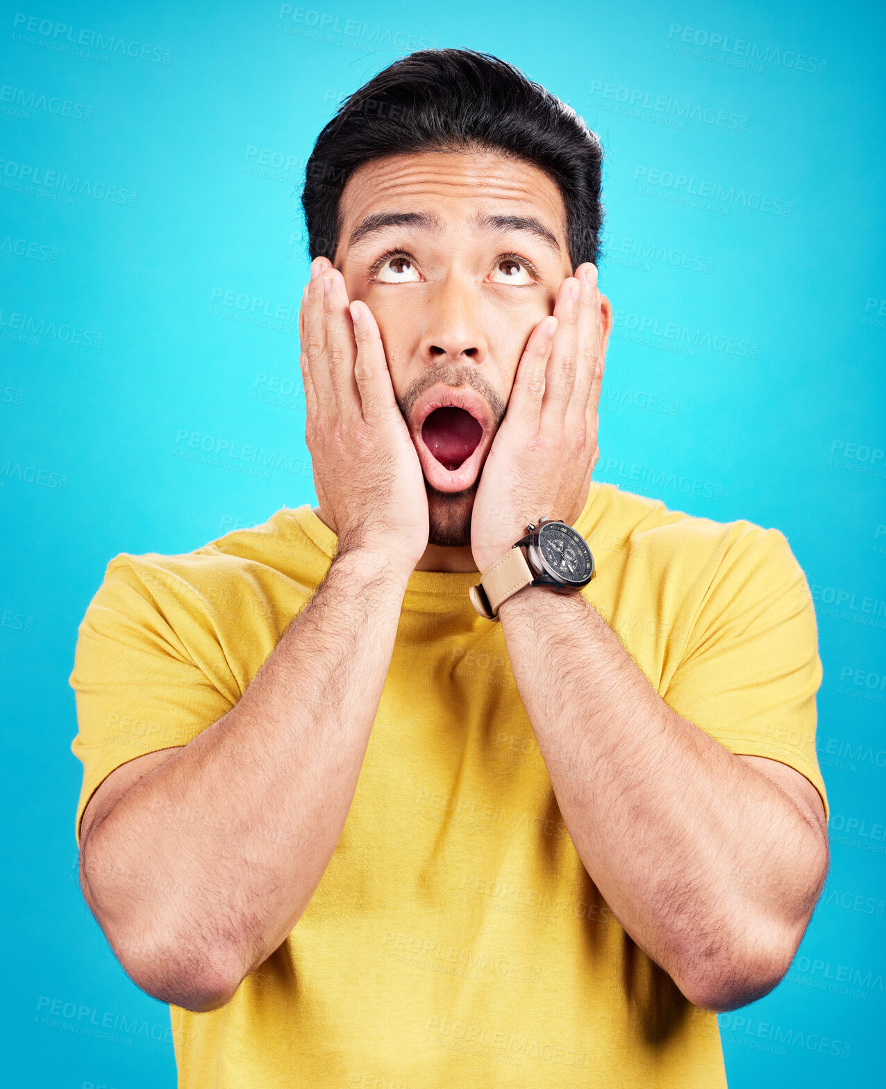 Buy stock photo Man, wow and shocked at surprise or announcement in studio with hands on face and mouth open. Male model person on a blue background while thinking of gossip, sale or promotion with comic emoji