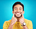 Teeth, smile and pointing with a man on a blue background in studio for dental care or oral hygiene. Portrait, face and happy with a handsome young male at the dentist for tooth care or whitening