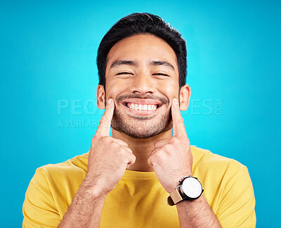 Buy stock photo Teeth, smile and pointing with a man on a blue background in studio for dental care or oral hygiene. Portrait, face and happy with a handsome young male at the dentist for tooth care or whitening