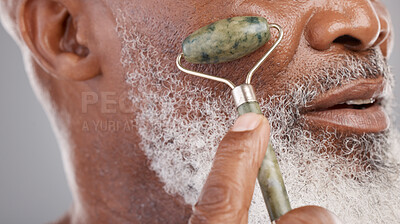 Buy stock photo Face roller, closeup and senior man with skincare, stone and dermatology product for skin glow. Elderly, cheek and facial roll of African male model doing self care for grooming with jade for beauty