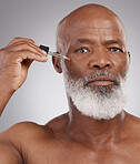 Skincare, portrait and man with face serum in a studio for a natural, beauty and skin treatment. Cosmetic, health and senior male model with facial oil for a wellness routine by a gray background.