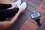 Phone, fitness and footwear from above with a woman athlete sitting on the ground to tie laces. Exercise, music and getting ready for running with a female sports person outdoor for cardio training