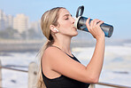 Music, fitness and woman drinking water at the beach for sports, running and cardio routine. Podcast, bottle and thirsty female runner relax on workout break while streaming online motivation track