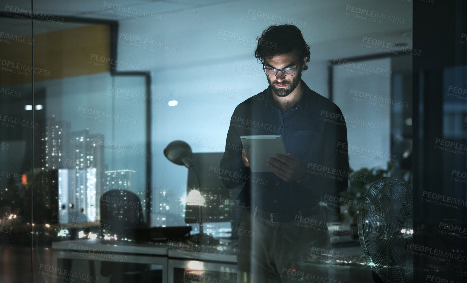 Buy stock photo Business man, tablet and serious in office, online browsing or web scroll by window with city lights at night. Technology, working late and professional person with touchscreen for research deadline.