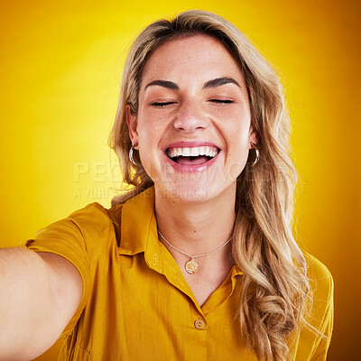 Buy stock photo Selfie, face and smile with a laughing woman on a yellow background in studio for fun or humor. Eye closed, comic and funny with an attractive young female model enjoying comedy, being silly or goofy