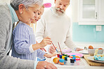 Easter, paint and a creative girl with her grandparents in their home for love, bonding or celebration together. Family, kitchen or egg with a senior couple and grandchild in a house for painting