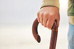 Hand, senior man with disability and cane or walking stick for support. Injury or osteoarthritis, physical therapy or rehabilitation and elderly male patient holding a wooden walk aid outside