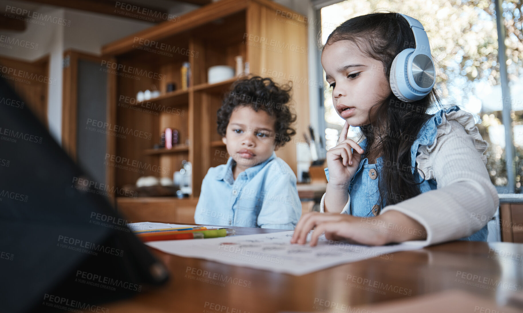 Buy stock photo Girl child, homework and thinking with headphones, music or little brother at desk in family home. School kids, study or confused with document for assessment, test or focus for education development