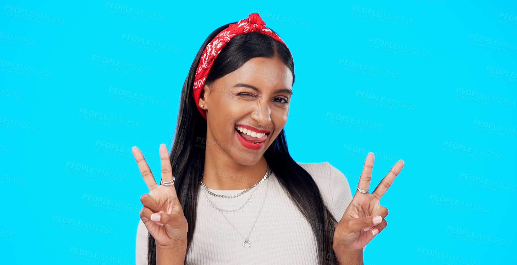 Buy stock photo Woman, portrait and wink with peace sign, happy with makeup and beauty isolated on blue background. Confidence, V and emoji, Indian model is goofy and cheerful with tongue out and fun in studio