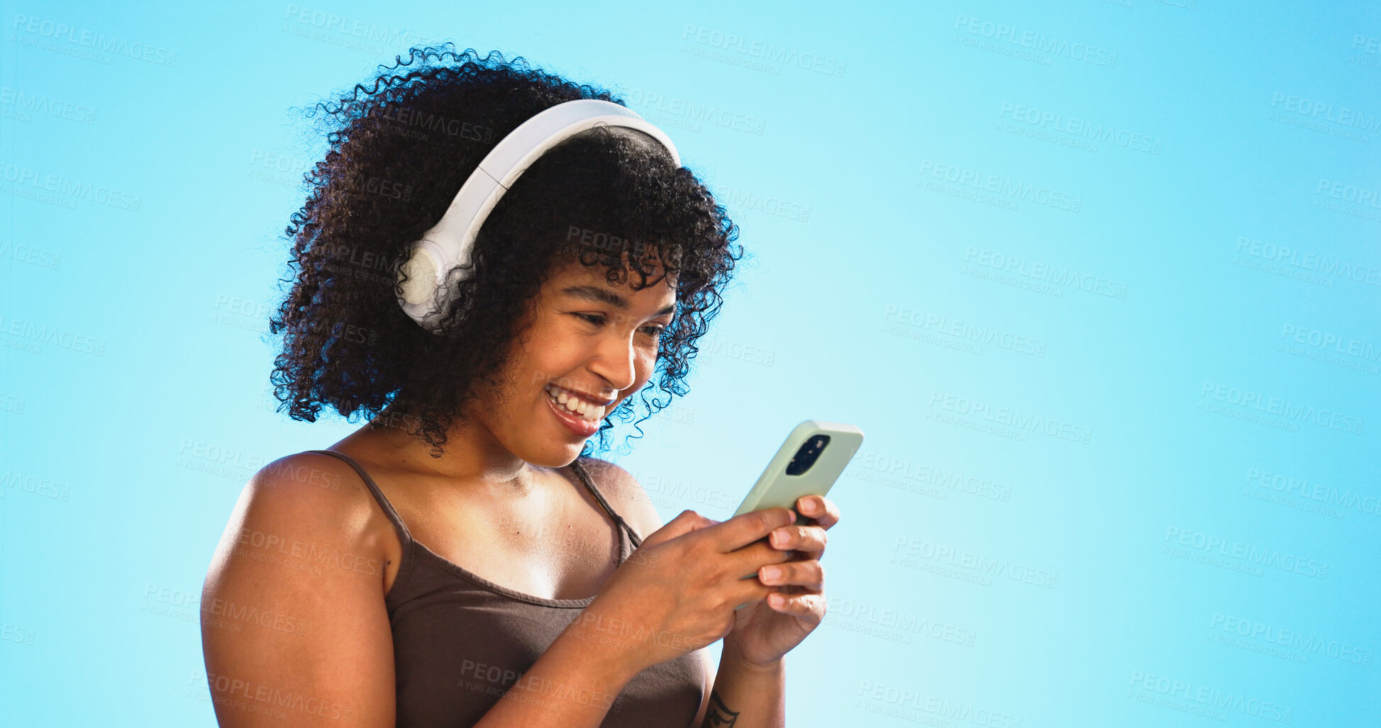 Buy stock photo Headphone, phone and happy woman on social media listening to music isolated in studio blue background. Funny, meme and person texting or chatting on internet post with audio, podcast or radio
