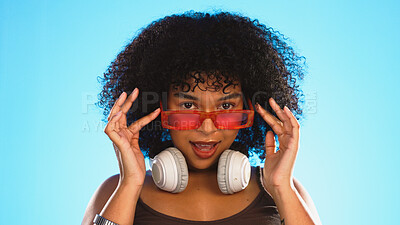 Trendy, gen z and face of a black woman in a studio with accessories, sunglasses and fashion. Happy, afro and portrait of African female model with a cool, stylish and edgy style by a blue background