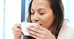 Woman drinking a hot cup of tea or coffee at home. Face of a carefree young female smelling the aroma of a fresh warm beverage while taking a sip and relaxing at home. Enjoying a comfortable break