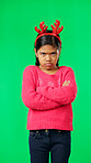 Portrait, christmas and an unhappy girl on a green screen background standing arms crossed in anger. Kids, sad and frustrated with a miserable little female child looking moody, annoyed or upset