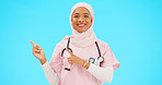 Woman doctor pointing to mockup isolated on blue background for healthcare presentation or product placement space. Happy face of nurse or medical muslim person show advertising mock up in studio