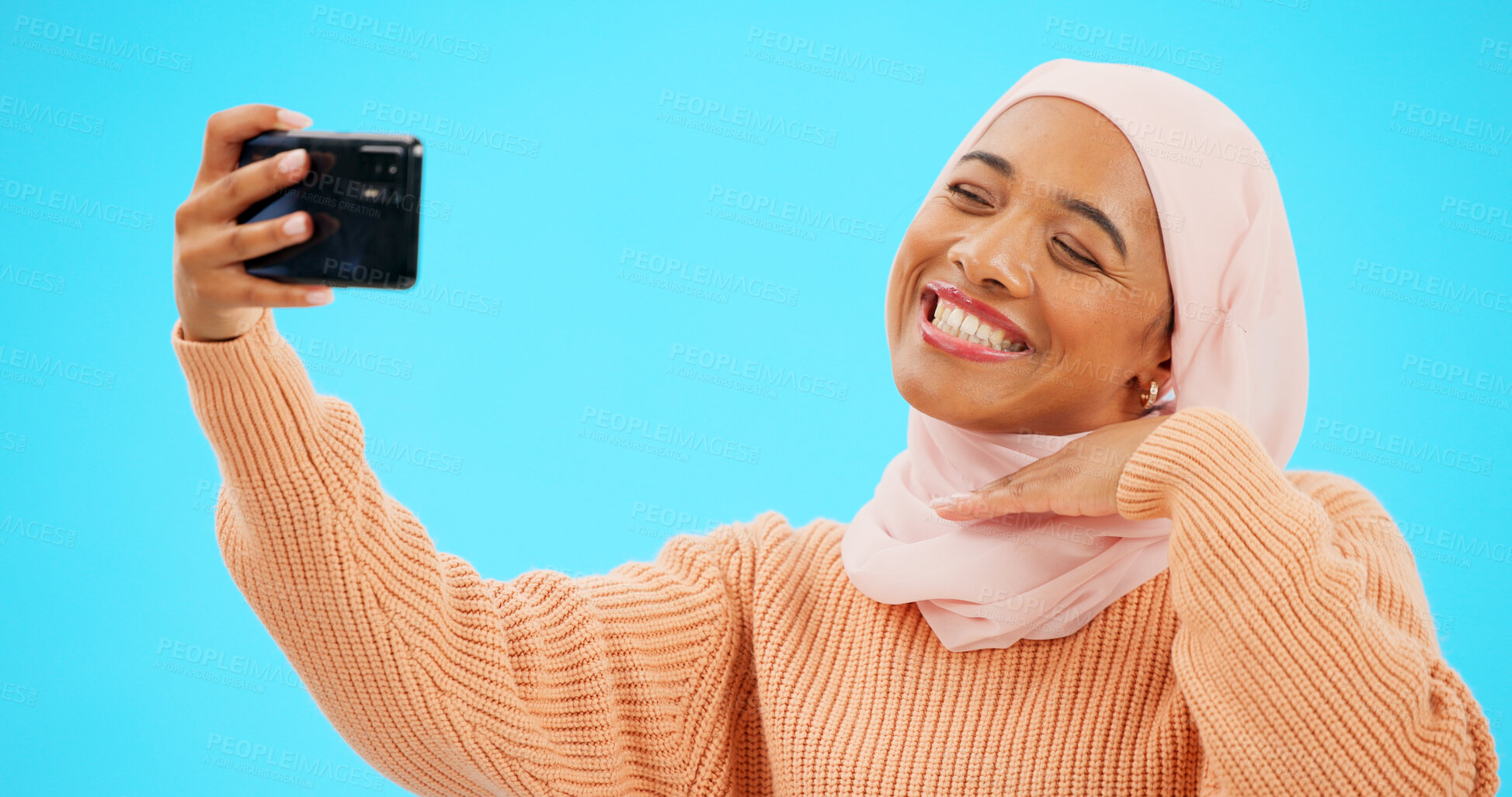 Buy stock photo Islamic woman, selfie and smile in studio for web blog, post or story on social media by blue background. Muslim influencer girl, hijab and fashion for memory, photography or profile picture update