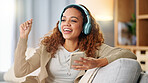 Woman wearing headphones and using a phone to listen to her music while relaxing on a sofa at home. Carefree female dancing and having fun alone on a couch, enjoying her free time on a weekend