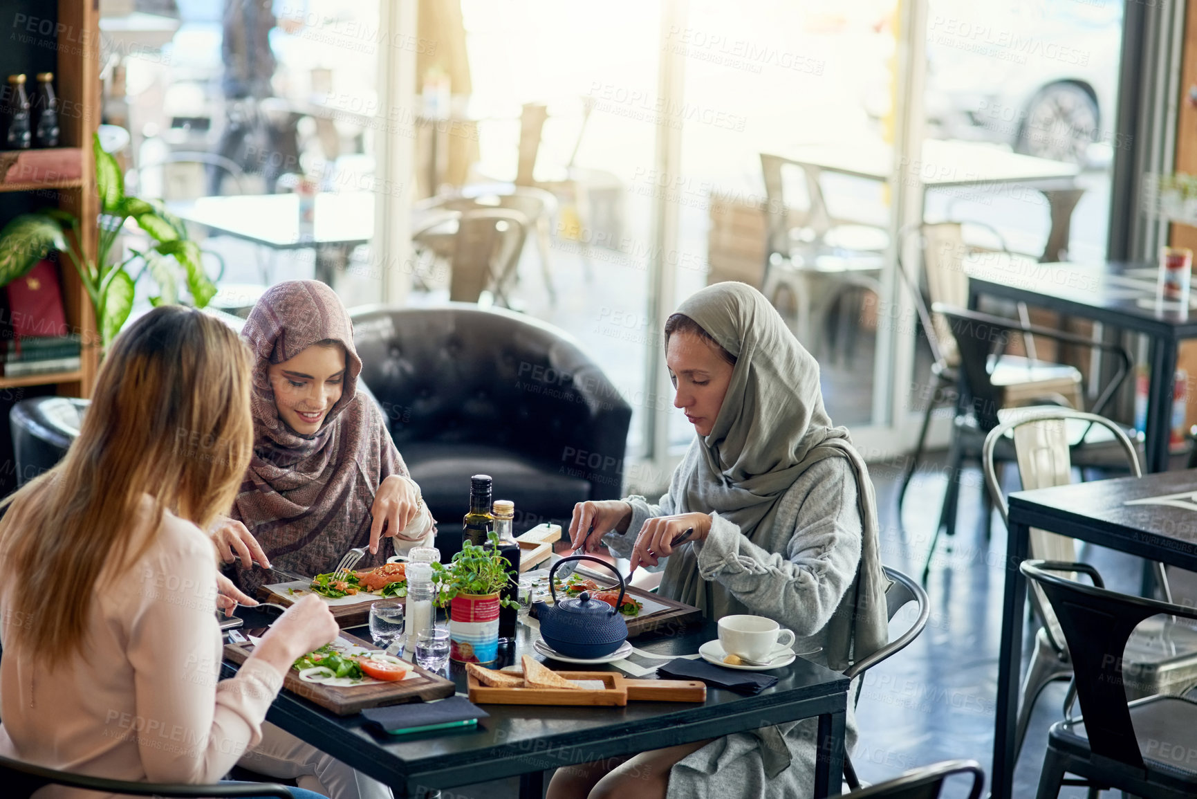 Buy stock photo Muslim women, talking and lunch in restaurant, together or friends with food, smile or happiness. Islamic woman, hungry group and brunch with social conversation, eating or listening to chat in cafe