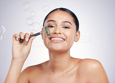 Buy stock photo Beauty, face roller and a woman in studio for skin glow, dermatology or natural cosmetics. Portrait of happy female model for facial massage and skincare benefits on bubbles and white background