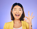 Portrait, smile and Asian woman with ok sign, wink and emoji against a studio background. Face, female person and model with happiness, hand gesture and symbol for thank you, perfect and approval
