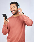 Man, smile and smartphone with headphones, listening to music or podcast isolated on studio background. Male person is enjoying radio streaming, online with wireless technology and playlist on app