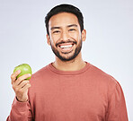 Man in portrait, apple and nutrition with health and diet with self care isolated on studio background. Male person with smile, green fruit and organic with healthy food, detox and lose weight