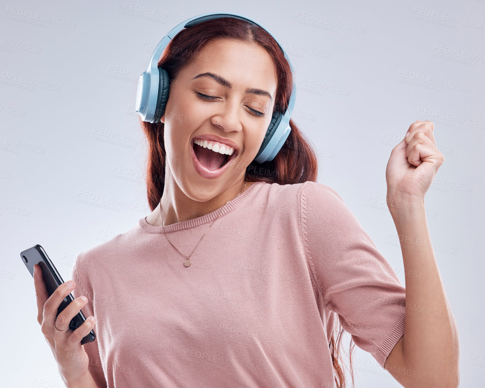 Buy stock photo Happy woman with mobile in headphones singing music or dancing to radio audio in studio on white background. Dance, smile or girl streaming or listening to song playlist in freedom with cellphone 