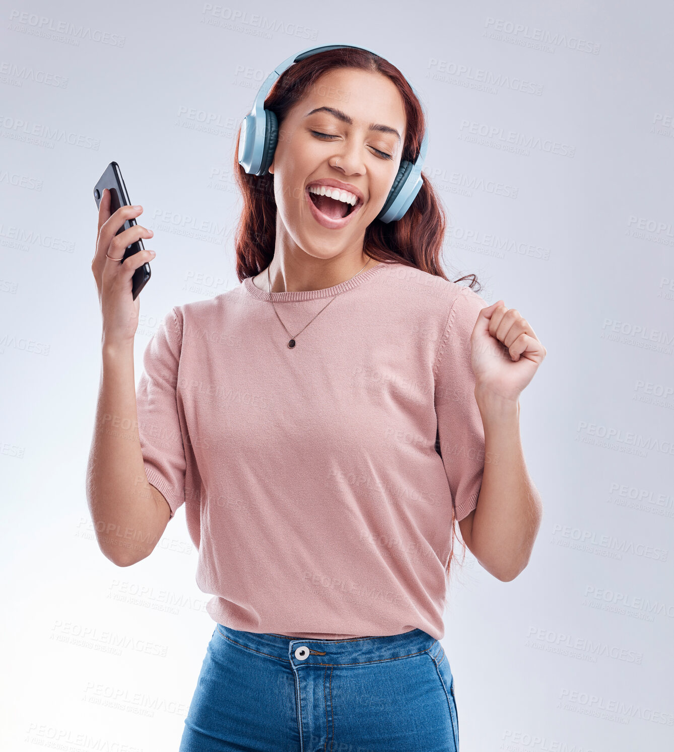 Buy stock photo Happy girl with mobile in headphones dancing music or singing a radio audio in studio on white background. Dance, smile or woman streaming or listening to song playlist in freedom with cellphone 