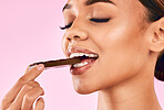 Happy woman, face and eating sweet chocolate, cocoa or delicious dessert against a pink studio background. Closeup of calm female mouth, lips or teeth biting and enjoying tasty sugar food or candy