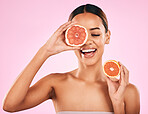 Happy woman, smile and grapefruit for vitamin C, nutrition or natural skincare against a pink studio background. Face of female person smiling with organic fruit for healthy diet, fiber or wellness