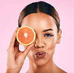 Woman, portrait and grapefruit on face for vitamin C nutrition or natural skincare against a pink studio background. Closeup of female person holding organic fruit in healthy diet, facial or wellness