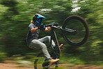 Fitness, trail and man doing a trick on a bike while riding for competition practice in the woods. Extreme sports, blur motion and male athlete biker with skill training or exercise in outdoor forest