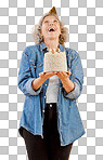 One happy mature caucasian woman wearing a birthday hat and holding a cake while confetti falls from above in the studio. Smiling white lady celebrating another year isolated on a png background