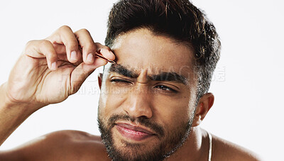 Man grooming his eyebrows with a tweezer in studio for self care, beauty and cleanliness. Hair removal, tweezing and male model from India doing facial epilation plucking routine by white background.