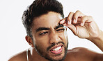 Man grooming his eyebrows with a tweezer in studio for self care, beauty and cleanliness. Hair removal, tweezing and male model from India doing facial epilation plucking routine by white background.