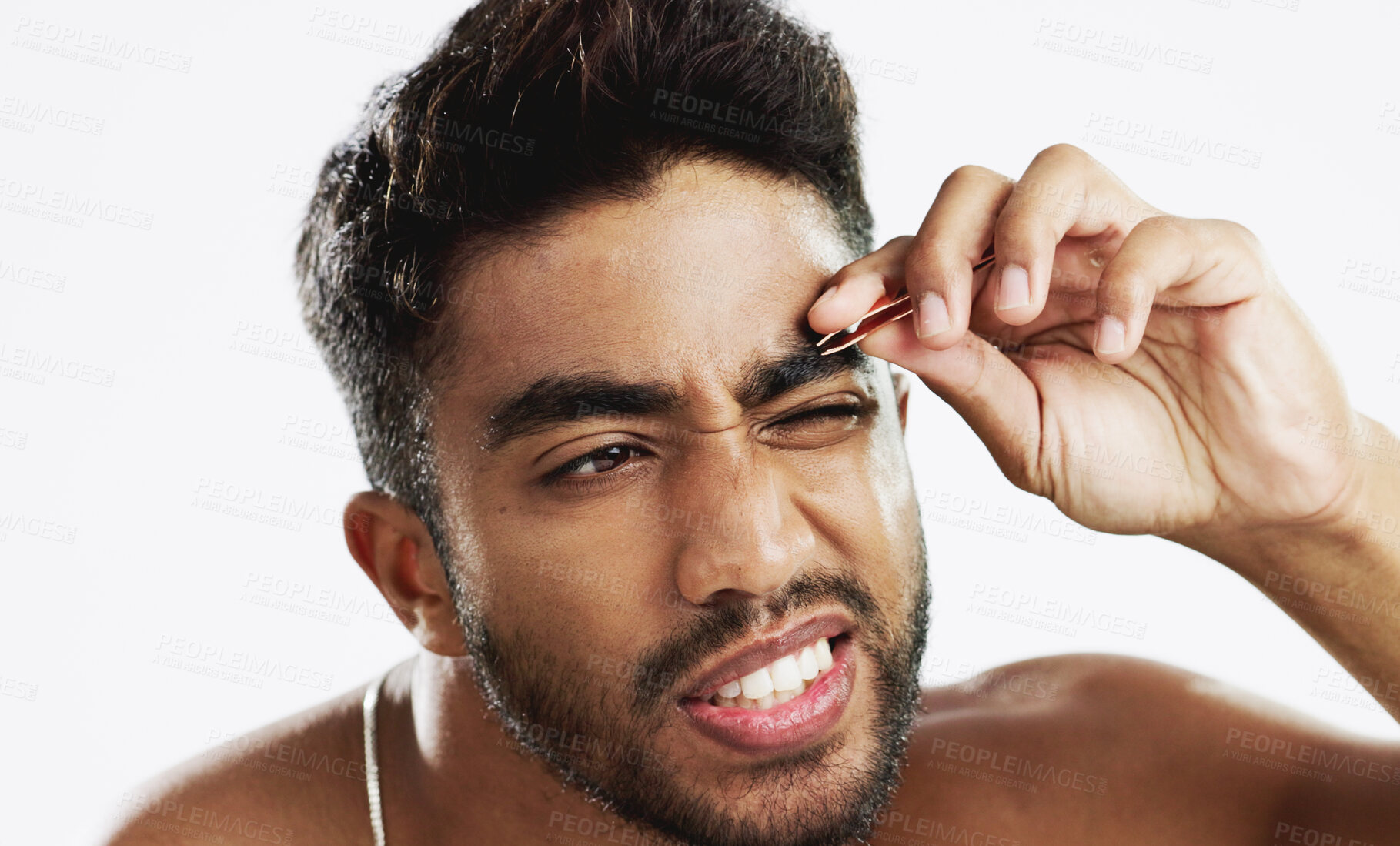 Buy stock photo Beauty, eyebrow and grooming with an indian man isolated on a white background in studio for his daily routine. Face, skincare and tweezer with a young person in pain to remove hair for wellness